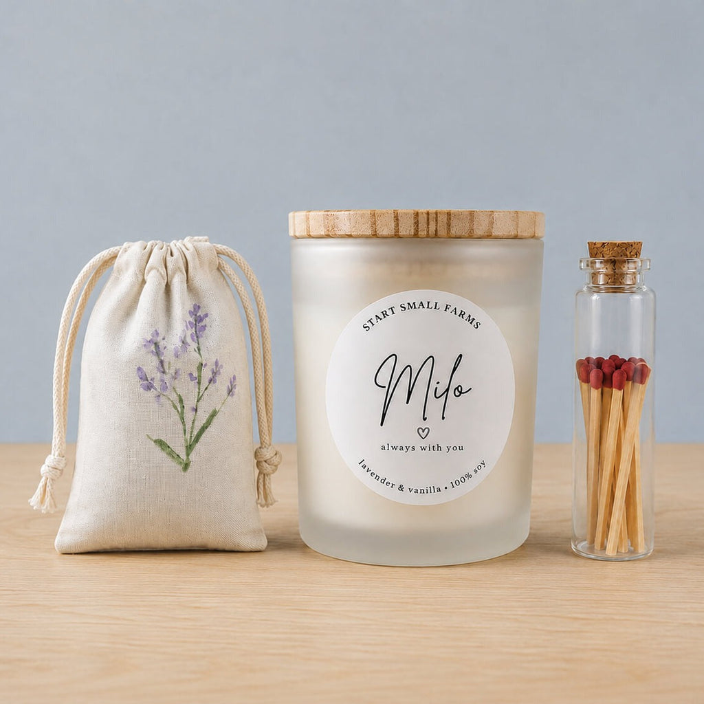 The Always With You set on a wood surface: a linen drawstring sachet hand-painted with a lavender sprig, a frosted soy candle with a bamboo lid labelled Milo, always with you, and a corked glass vial of red-tipped matches