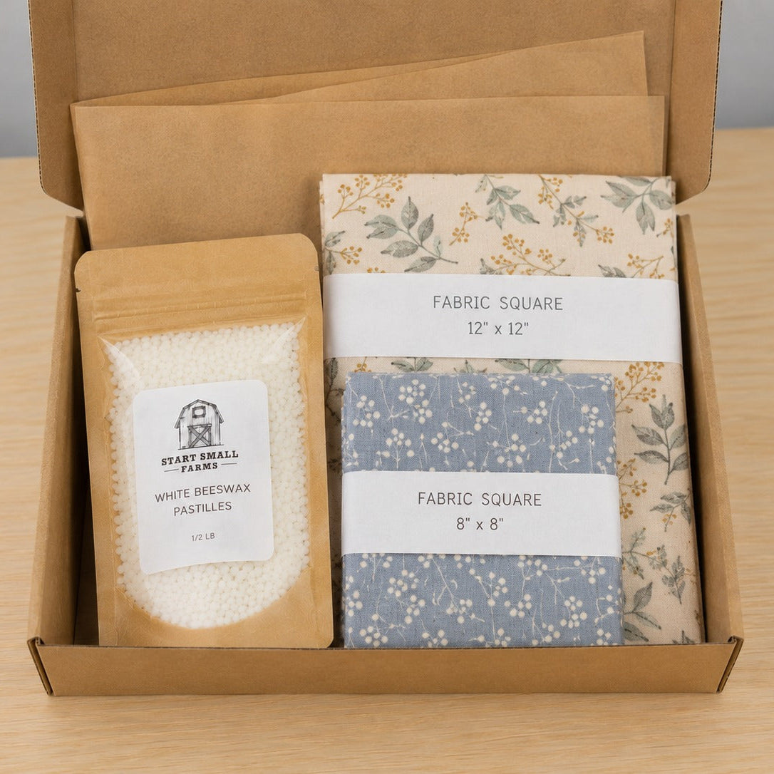 An open kraft box holding a pouch of white beeswax pastilles with a Start Small Farms label, a 12 by 12 inch botanical cotton square, and an 8 by 8 inch blue floral cotton square