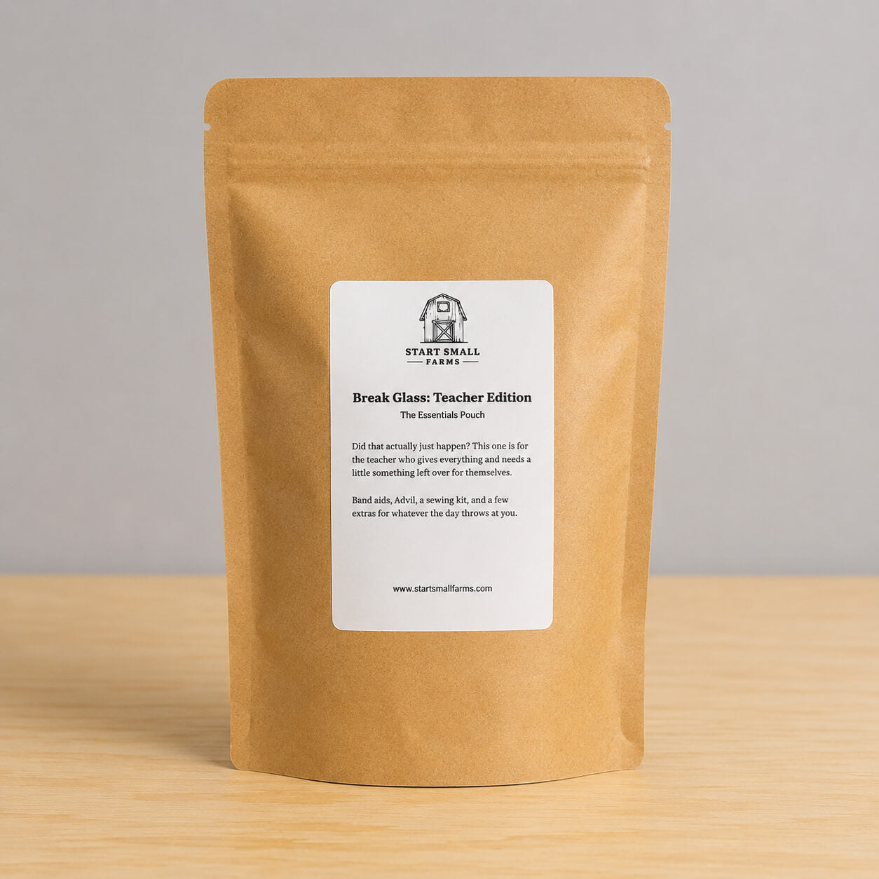 A stand-up kraft paper pouch with a white front label reading 'START SMALL FARM' and 'Break Glass: Teacher Edition,' photographed on a light wood surface against a plain light gray background.