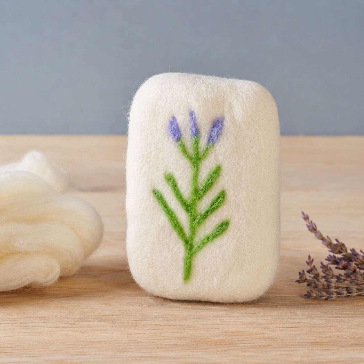 A finished felted bar with a needle felted lavender sprig in purple and green, a braid of cream roving and dried lavender beside it