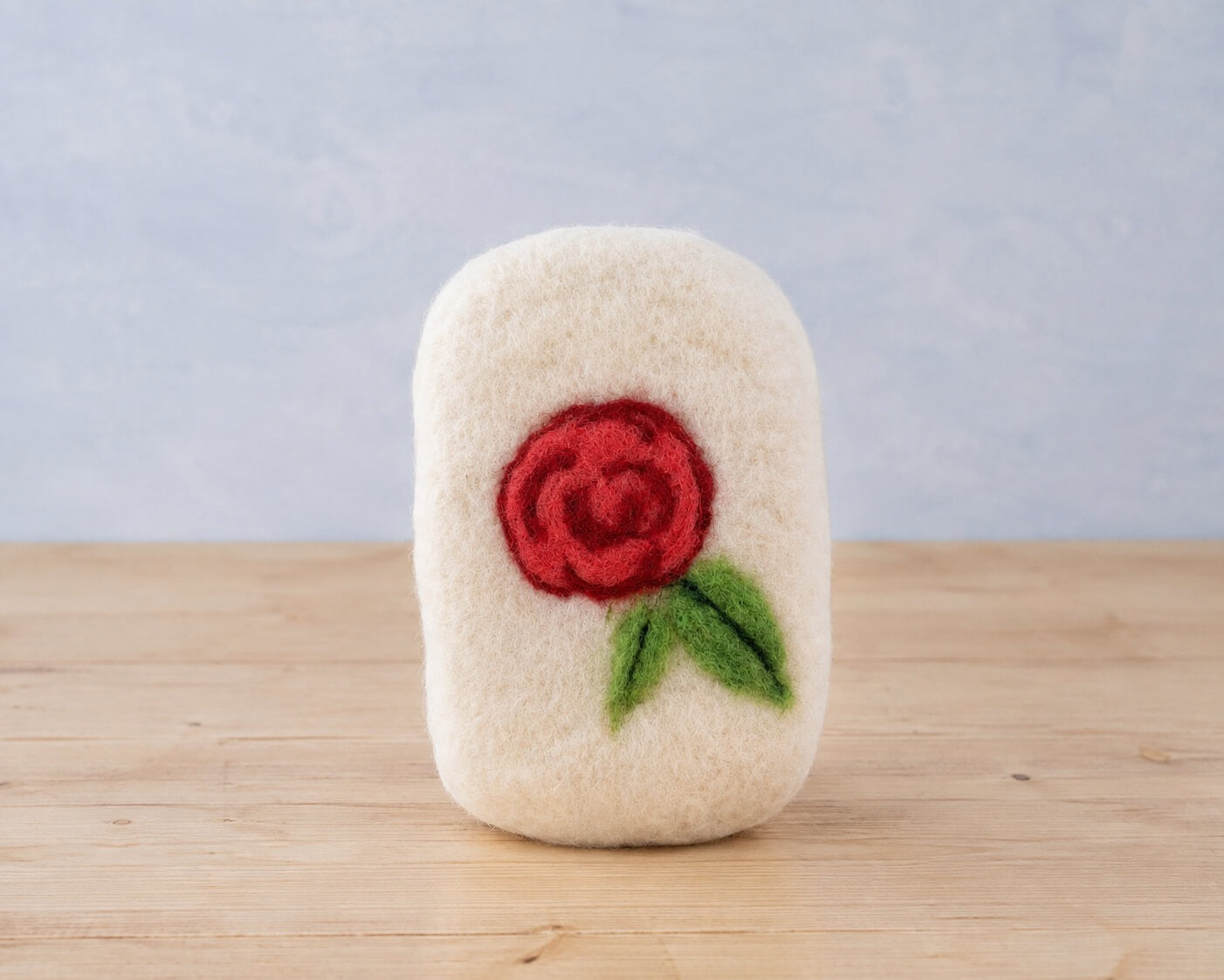 A finished felted bar with a red needle felted rose and two green leaves worked into the wool