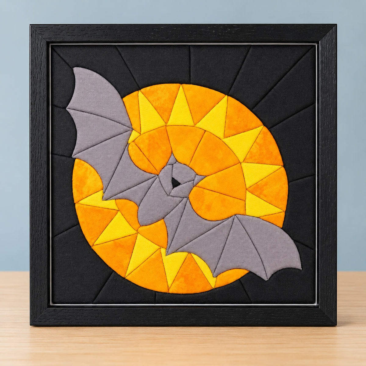 The same bat and moon design in a black frame, standing on a light wood table.