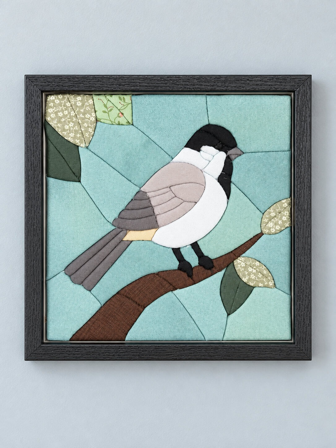 The same chickadee design in a black frame, hanging flat against a pale grey wall.