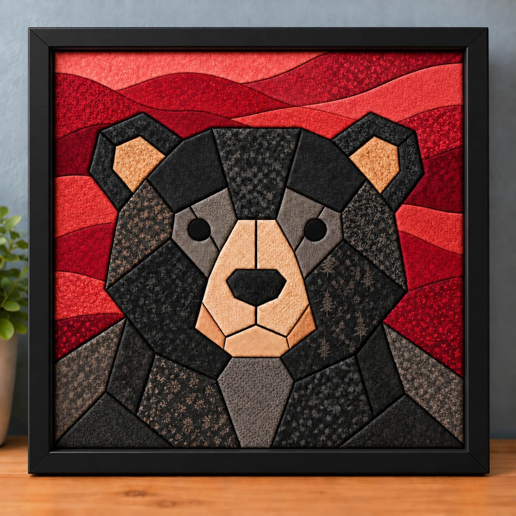 A chunky black bear kinusaiga piece in a black frame, standing on a wooden shelf against a blue-grey wall: a round geometric bear face in black and charcoal print fabrics, with grey around the eyes, a tan muzzle and ears, and a black nose, in front of rolling hills pieced in reds and coral.