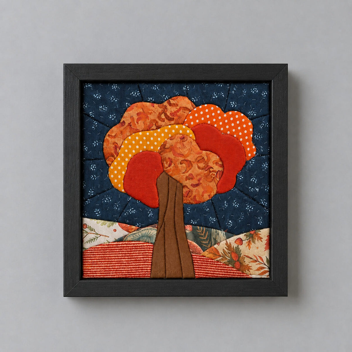The same fall tree design in a black frame, hanging flat against a light grey wall.