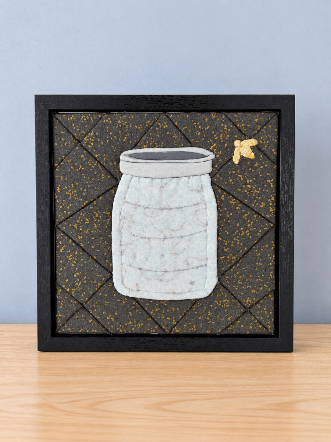 The same firefly jar design in the black frame with the lights switched off, so the jar reads as plain pale grey quilted fabric.
