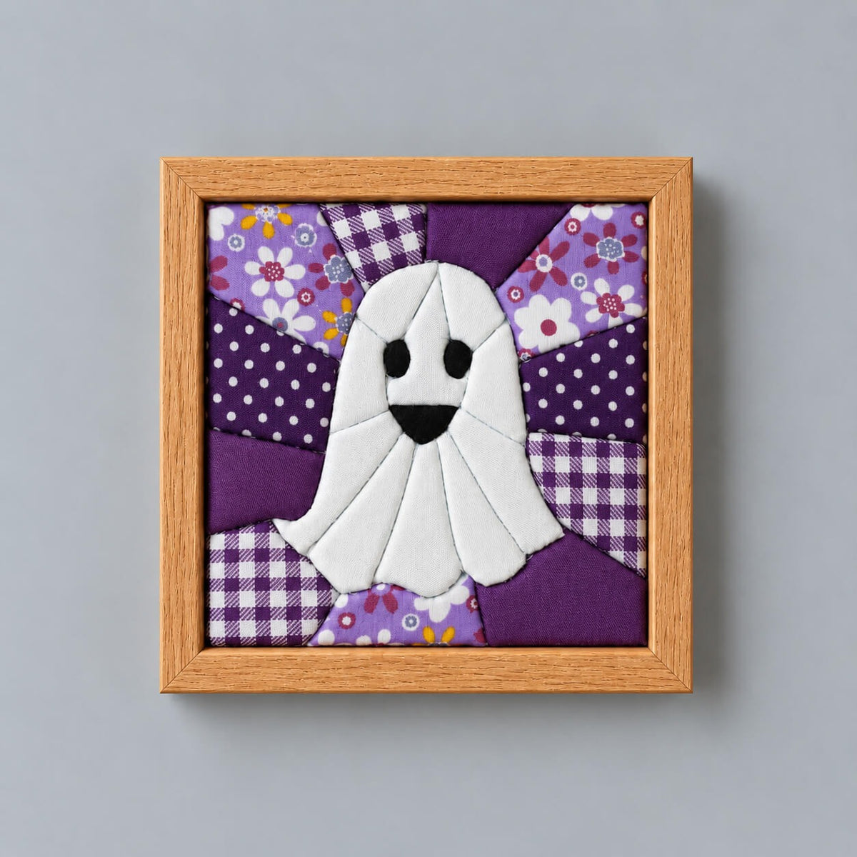 The same ghost design in a natural wood frame, hanging flat against a grey wall.