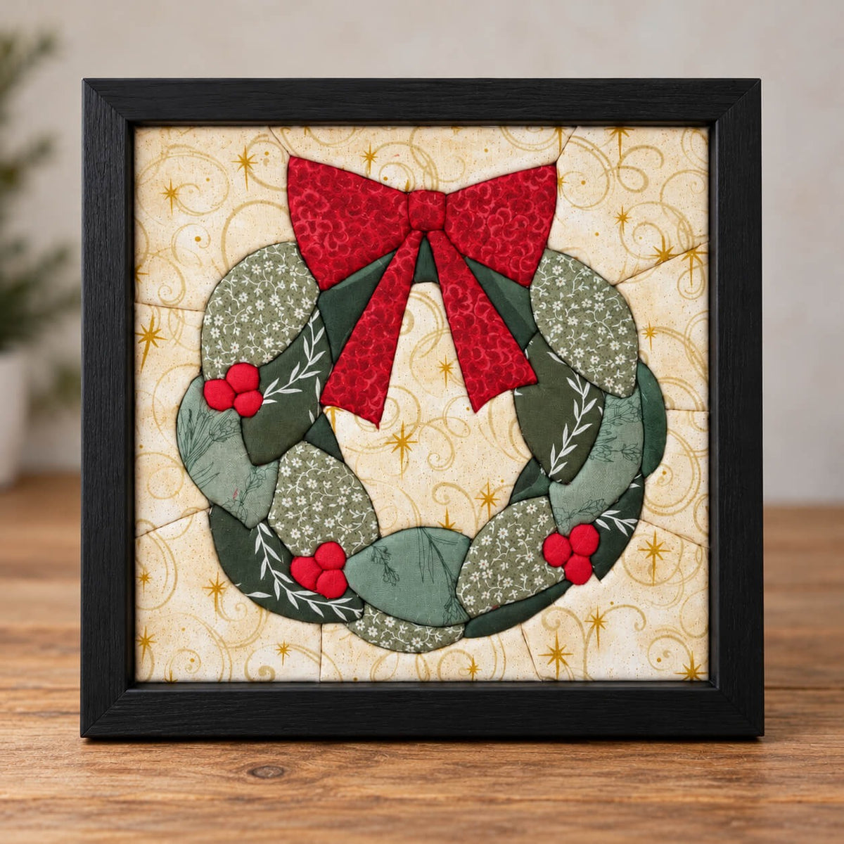 The same holiday wreath design in a black frame, standing on a wooden table.