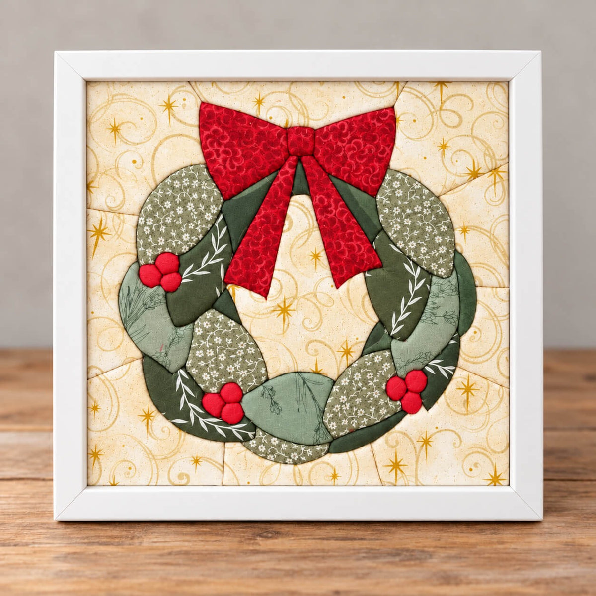 The same holiday wreath design in a white frame, standing on a wooden table.