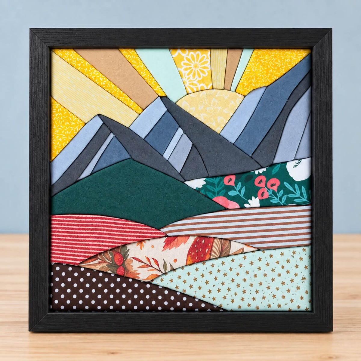 The mountain design in a black frame, standing on a light wood table against a grey-blue wall.