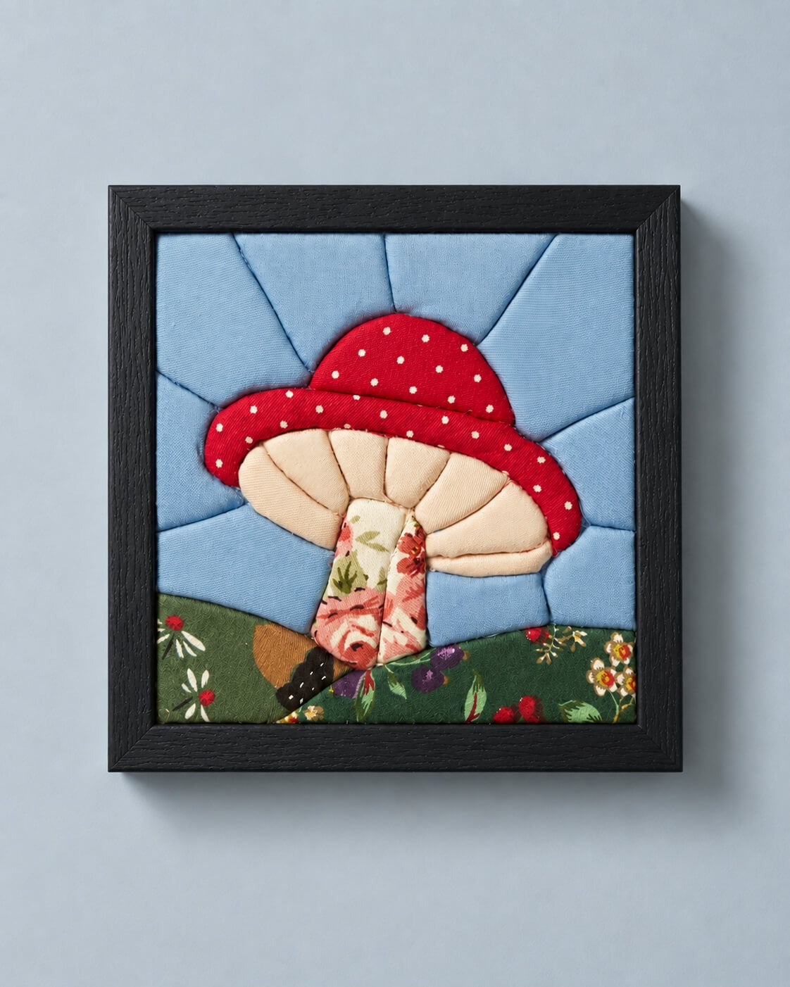The same mushroom design in a black frame, hanging flat on a grey-blue wall.