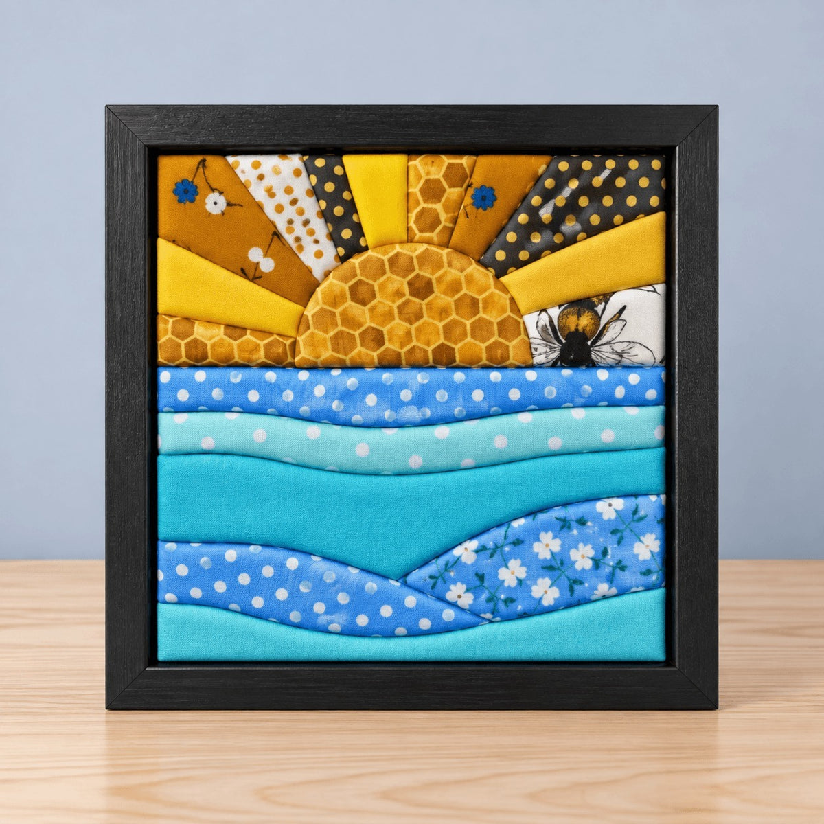 The same sun and waves design in a black frame, standing on the same light wood table.