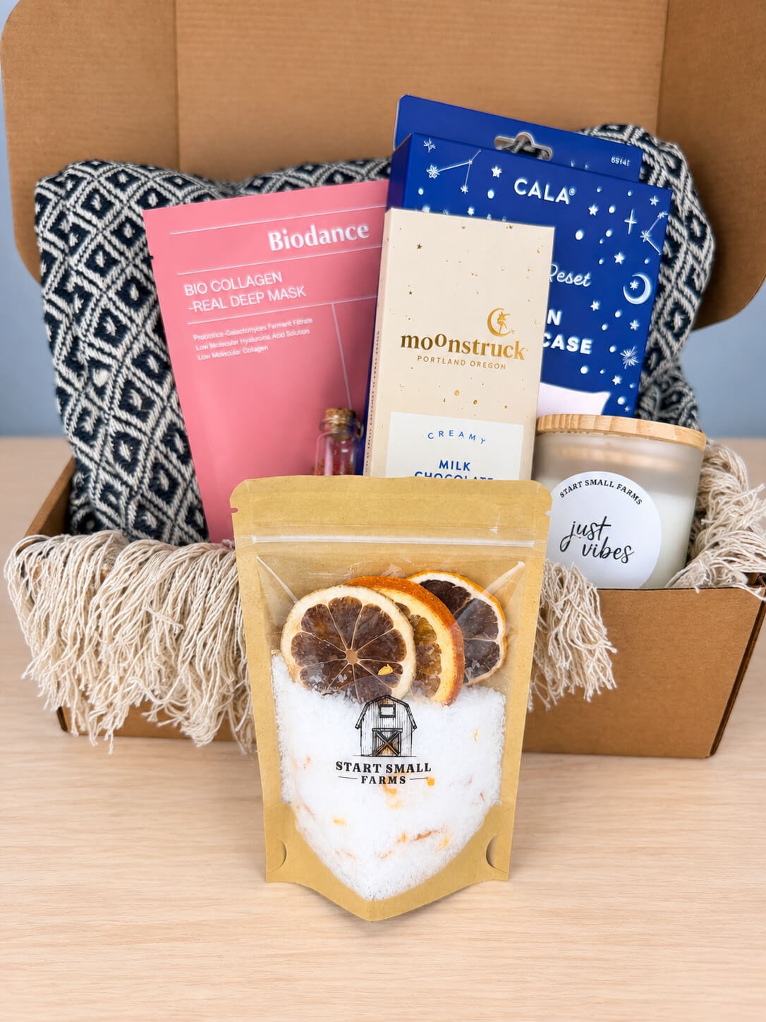 The Start Small Farms bath soak pouch standing in front of the open box, dried orange and lemon slices showing through the window above the salts.