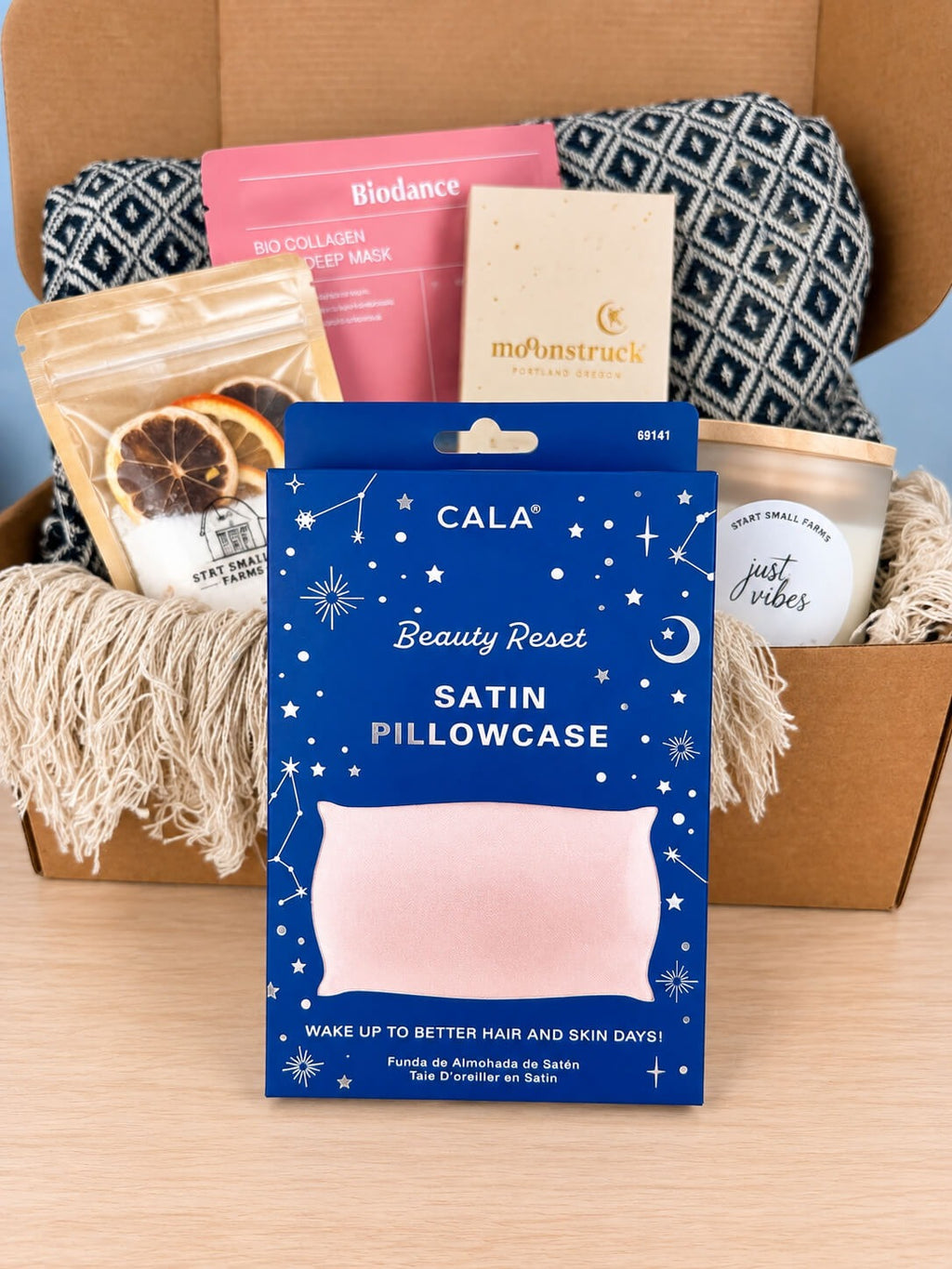 The CALA Beauty Reset satin pillowcase in its navy constellation box, pink satin showing through the window, in front of the open box.