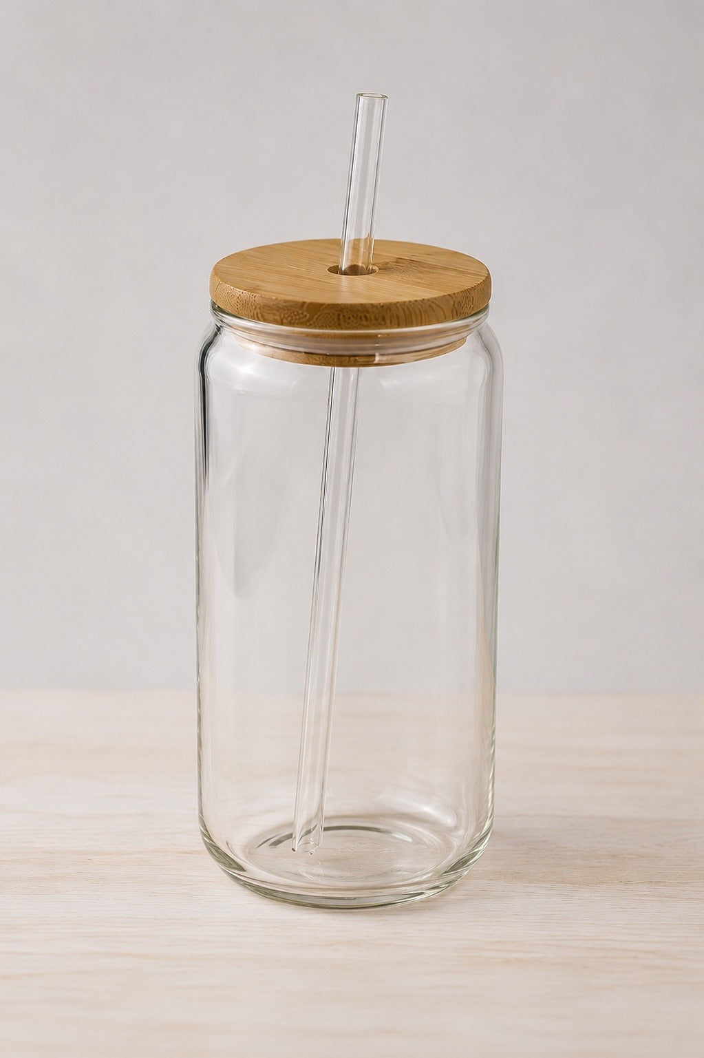 The 16oz glass tumbler with a bamboo lid and a glass straw, on pale wood