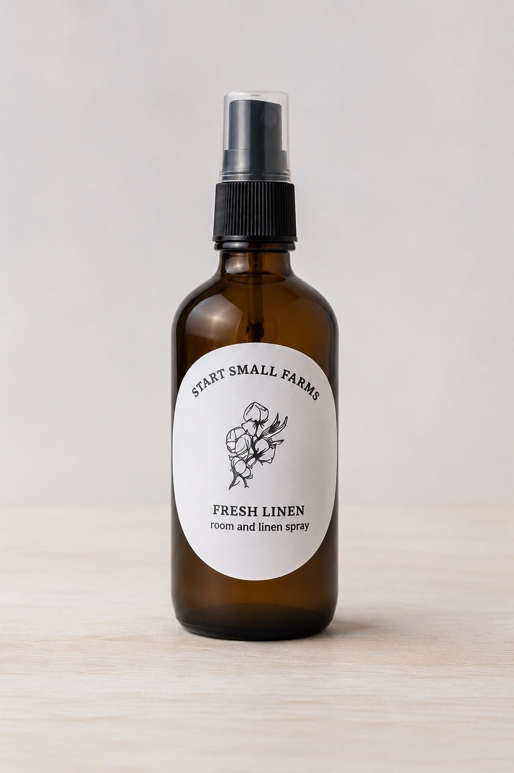 The Start Small Farms Fresh Linen room and linen spray in an amber glass bottle with a black mist top and a cotton-branch label