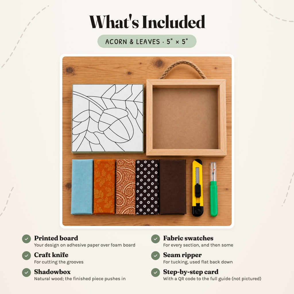 What's included in the Acorn & Leaves kit, laid out on a wood table: the printed acorn board, five fabric swatches in soft blue, burnt orange, brown paisley, polka dot and chocolate brown, a craft knife, a seam ripper and the natural wood shadowbox with its rope hanger. The step-by-step card is not pictured.