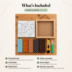 What's included in the Acorn & Leaves kit, laid out on a wood table: the printed acorn board, five fabric swatches in soft blue, burnt orange, brown paisley, polka dot and chocolate brown, a craft knife, a seam ripper and the natural wood shadowbox with its rope hanger. The step-by-step card is not pictured.