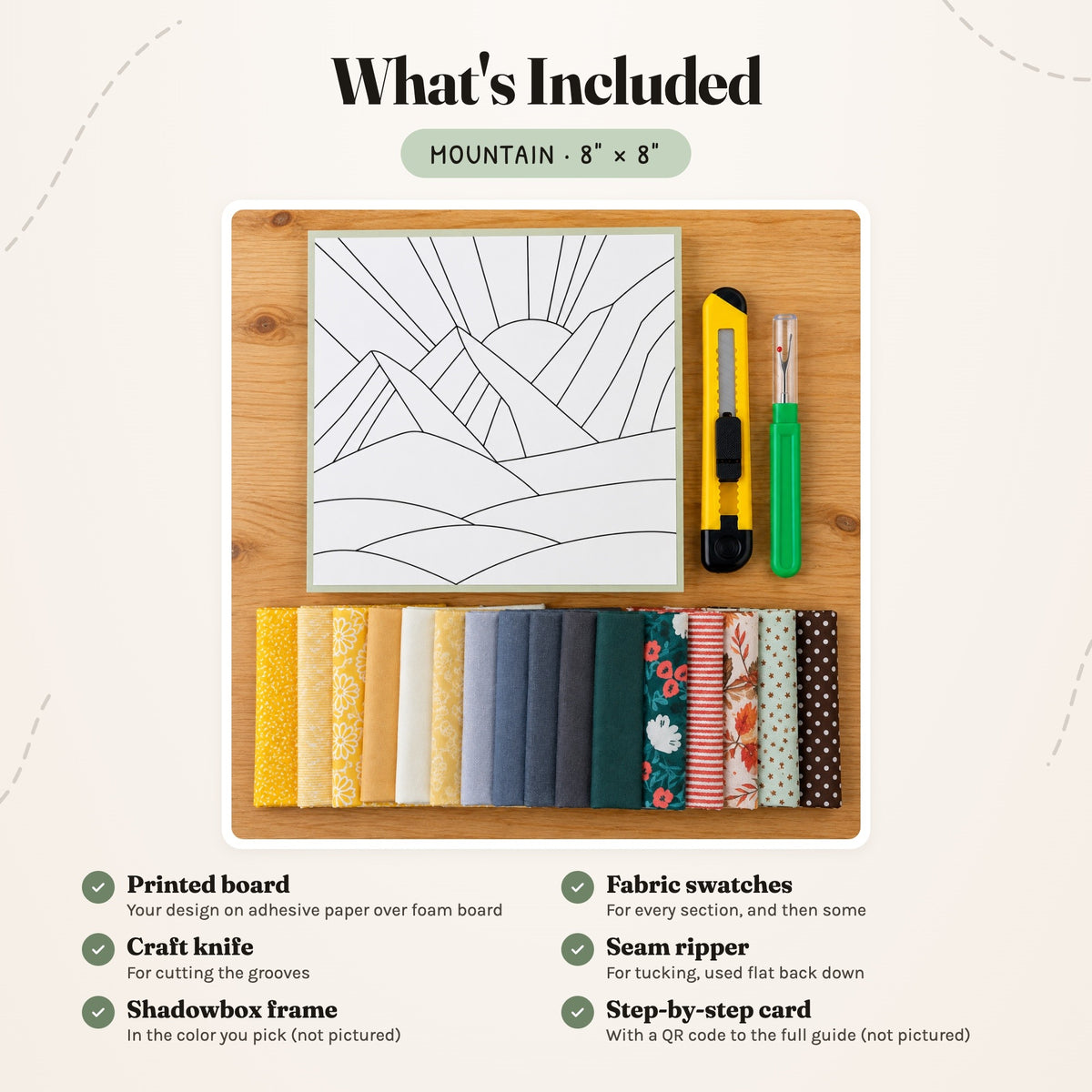 What's included in the Mountain kit, laid out on a wood table: the printed board, fabric swatches, a craft knife and a seam ripper. The shadowbox frame and the step-by-step card are not pictured.