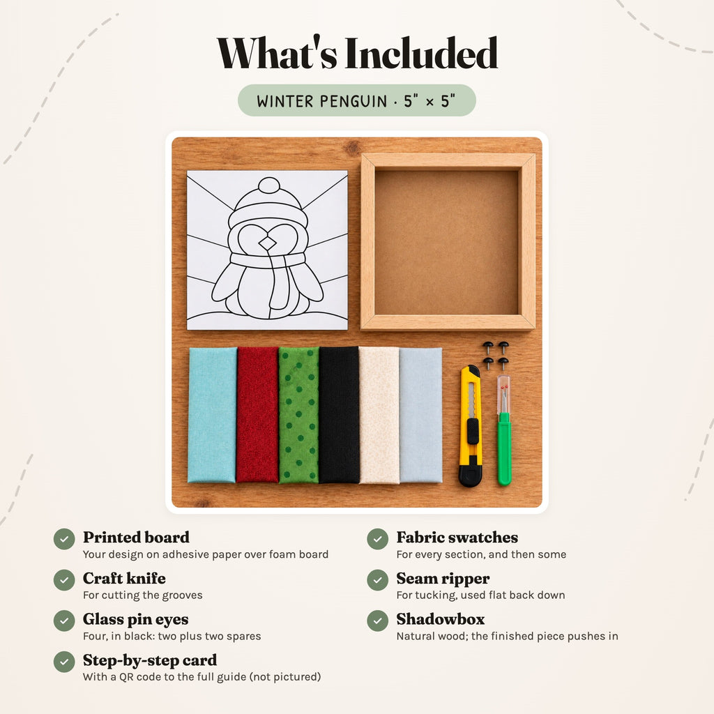 What's included in the Winter Penguin kit, laid out on a wood table: the printed penguin board, six fabric swatches in aqua, red, green polka dot, black, cream and pale blue, a craft knife, a seam ripper, four black glass pin eyes and the natural wood shadowbox. The step-by-step card is not pictured.