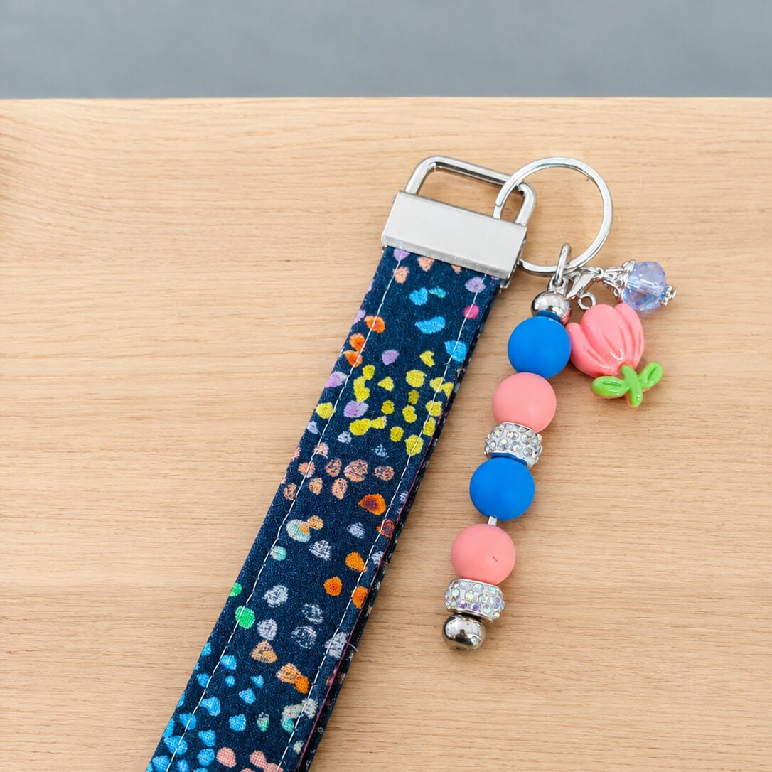 Close up of a finished wristlet in navy confetti print quilting cotton, with a silver clasp and split ring and a beaded bar ending in a pink flower charm