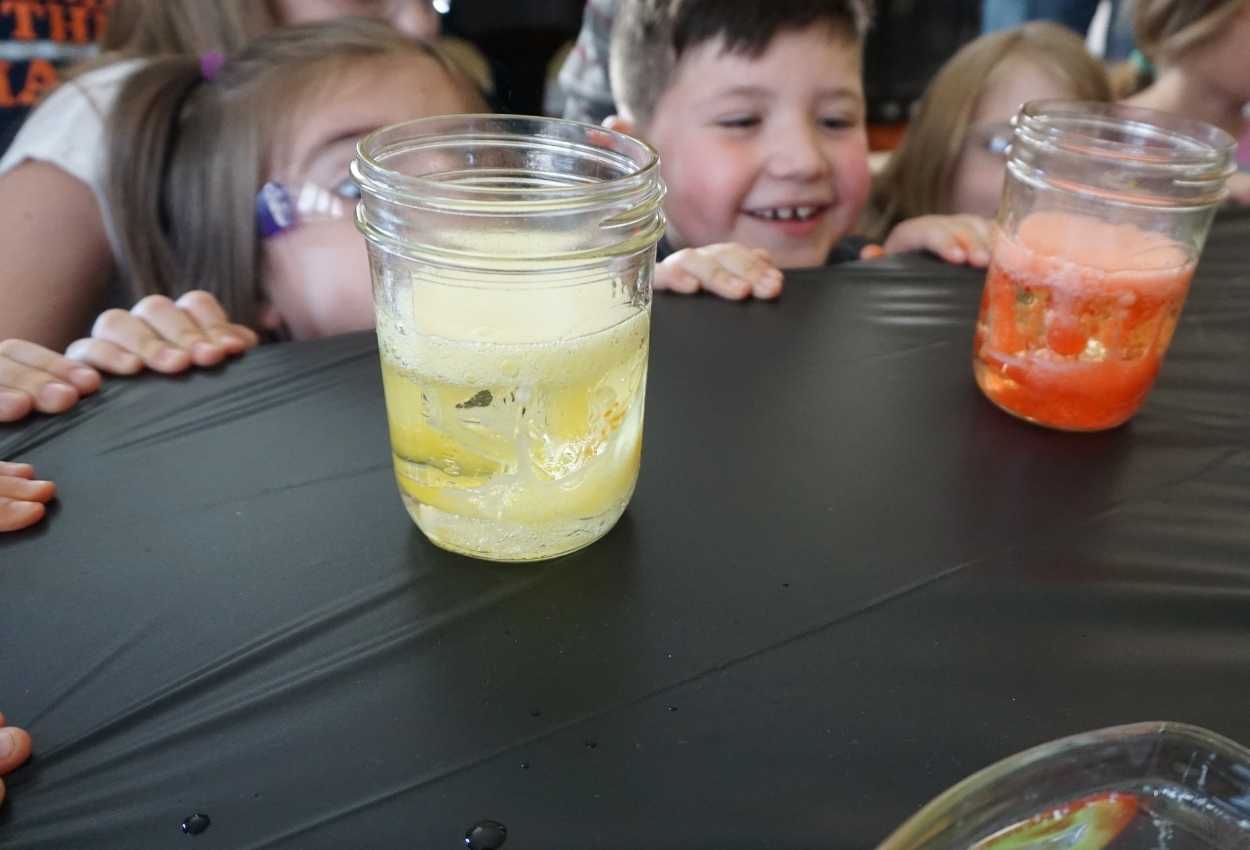 A photo of my son Isaac at a mad scientist themed birthday party with a glass jar of frozen cubes with baking soda and food coloring.