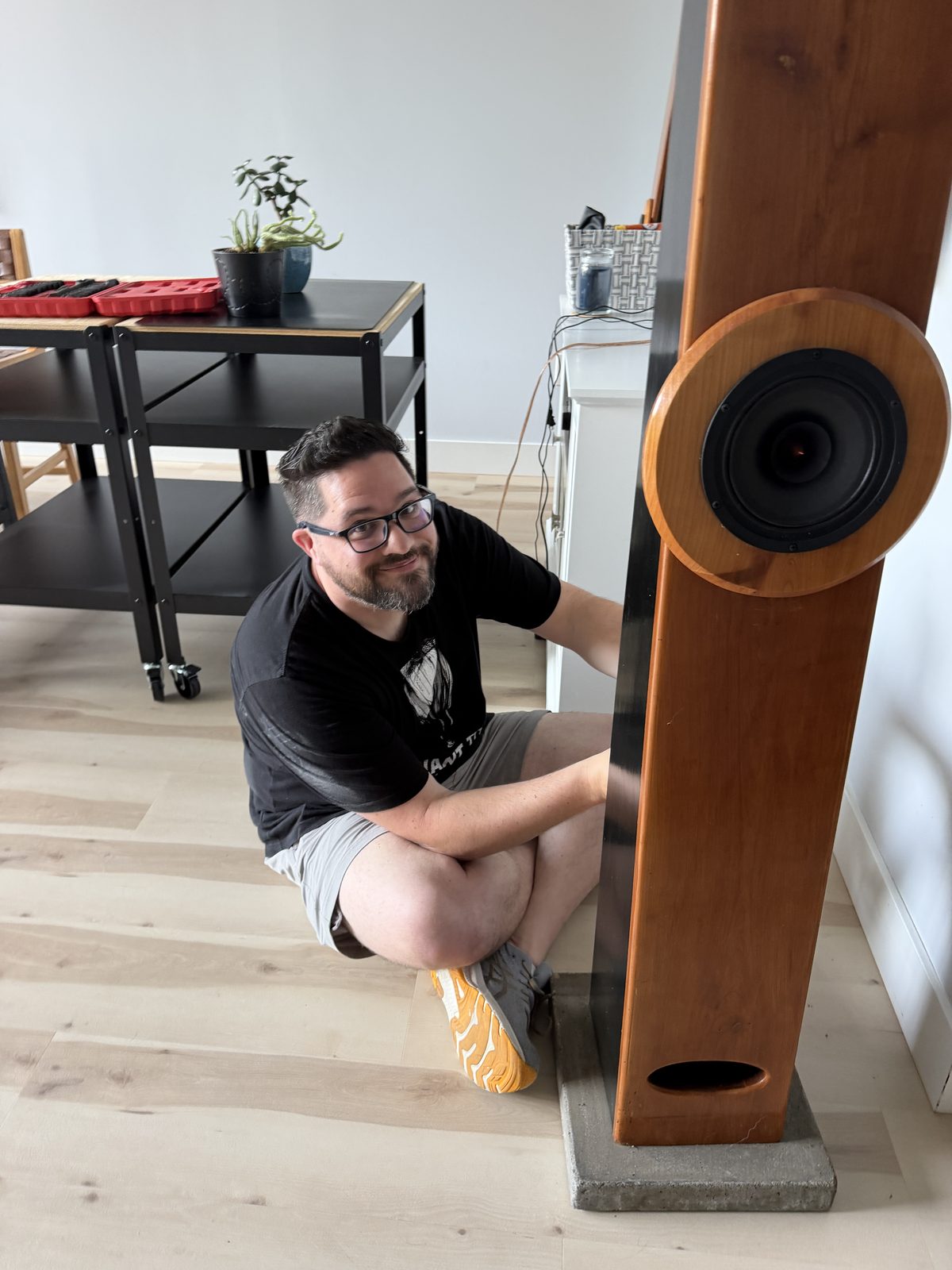 Jason kneeling beside a tall, tapered cherry-wood Voigt pipe speaker cabinet with a single large driver near the top.