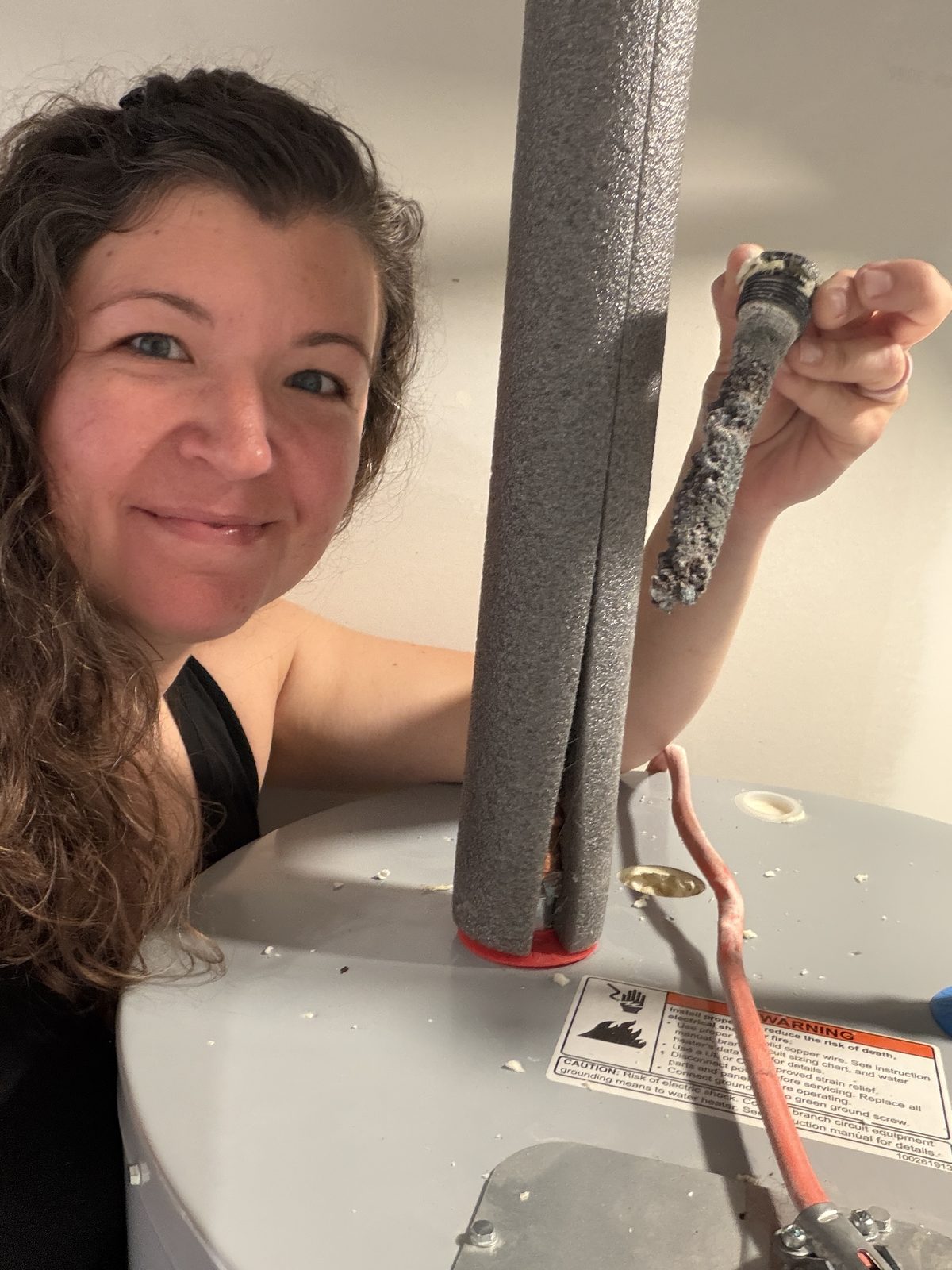 Kim smiling and holding up a heavily corroded, crusty anode rod she removed from the water heater.